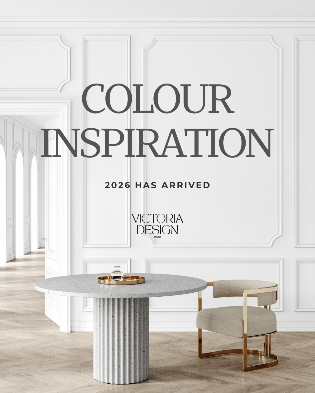 Text on a white wall reading 'Colour Inspiration 2026 Has Arrived' and 'Victoria Design Studio', with a modern round table and a beige chair in a bright, elegant room with wooden flooring.