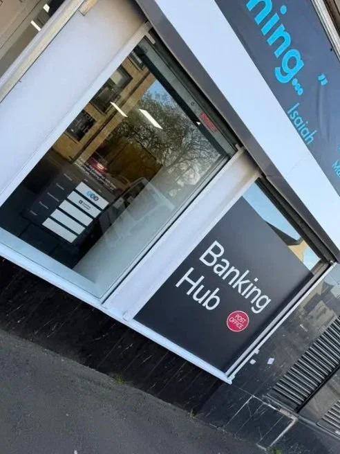 A storefront window with a sign that reads 'Banking Hub' and a pink circle with the text 'mobi'. The window reflects some trees and buildings outside.