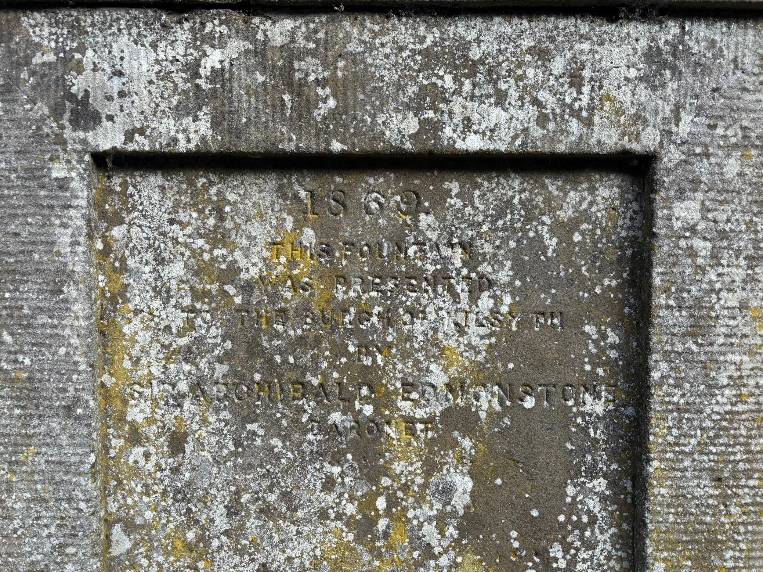 Close-up of a weathered gravestone with moss and lichen, with engraved text that reads 'In loving memory of Harold, dear son and brother'.
