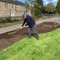 Person working on gardening or landscaping, digging or planting in a garden bed along a grassy area.