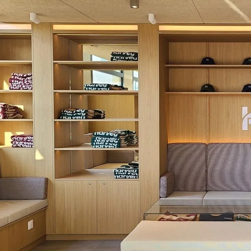 Étagères en bois avec des vêtements et casquettes, coin salon avec canapé et table en verre, décor moderne et lumineux.