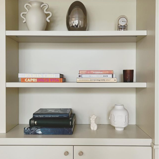 Étagère blanche avec livres, vases et une petite figurine en céramique.