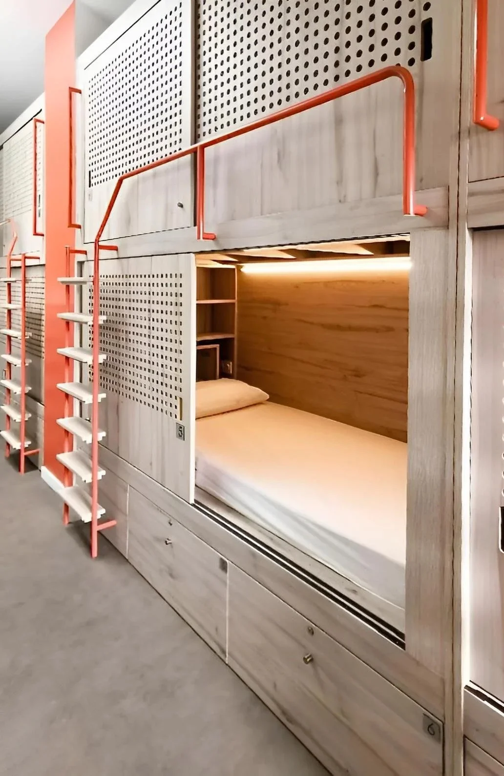 Lits en dortoir avec escaliers en bois et cadres métalliques orange dans une chambre d'auberge ou d'hôtel moderne.