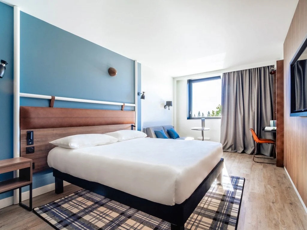 Chambre d'hôtel avec lit, canapé, bureau, mur bleu et rideaux gris.