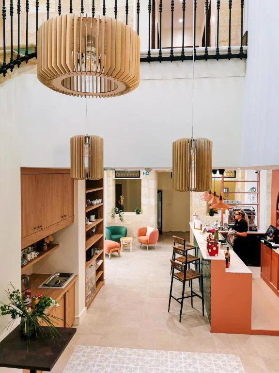 Vue intérieure d'un café ou d'un espace lounge avec des lampes en bois suspendues, un comptoir avec une personne, et des sièges colorés.