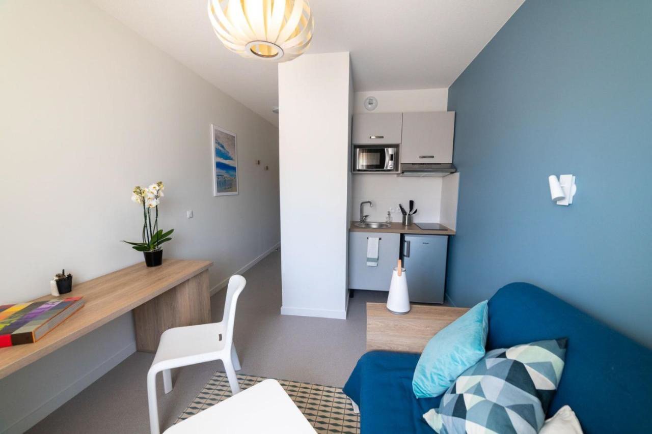 Petit appartement avec coin cuisine modern, canapé bleu avec coussins, bureau en bois avec une plante orchidée, tableau décoratif sur le mur, lampadaire blanc et jaune