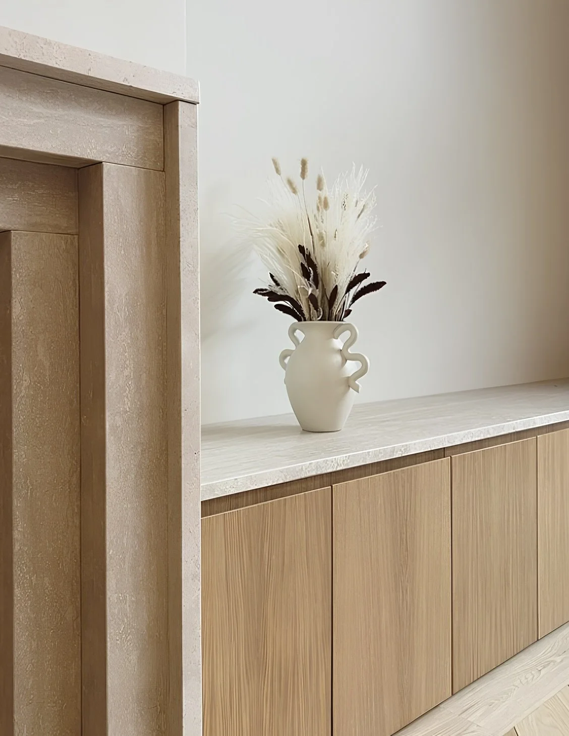Une vase blanche avec des fleurs séchées blanches et brunes placée sur un meuble en bois au bureau.