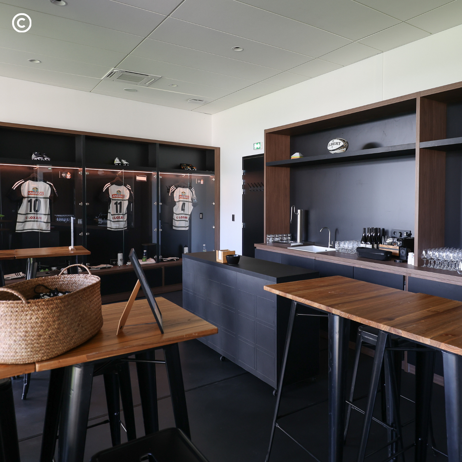 Salle de réception sportive avec affiches, vêtements et trophées de rugby, bar avec verres et bouteilles.