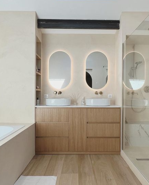 Salle de bain moderne avec deux lavabos, miroirs avec éclairage intégré, cabine de douche en verre et éléments en bois.