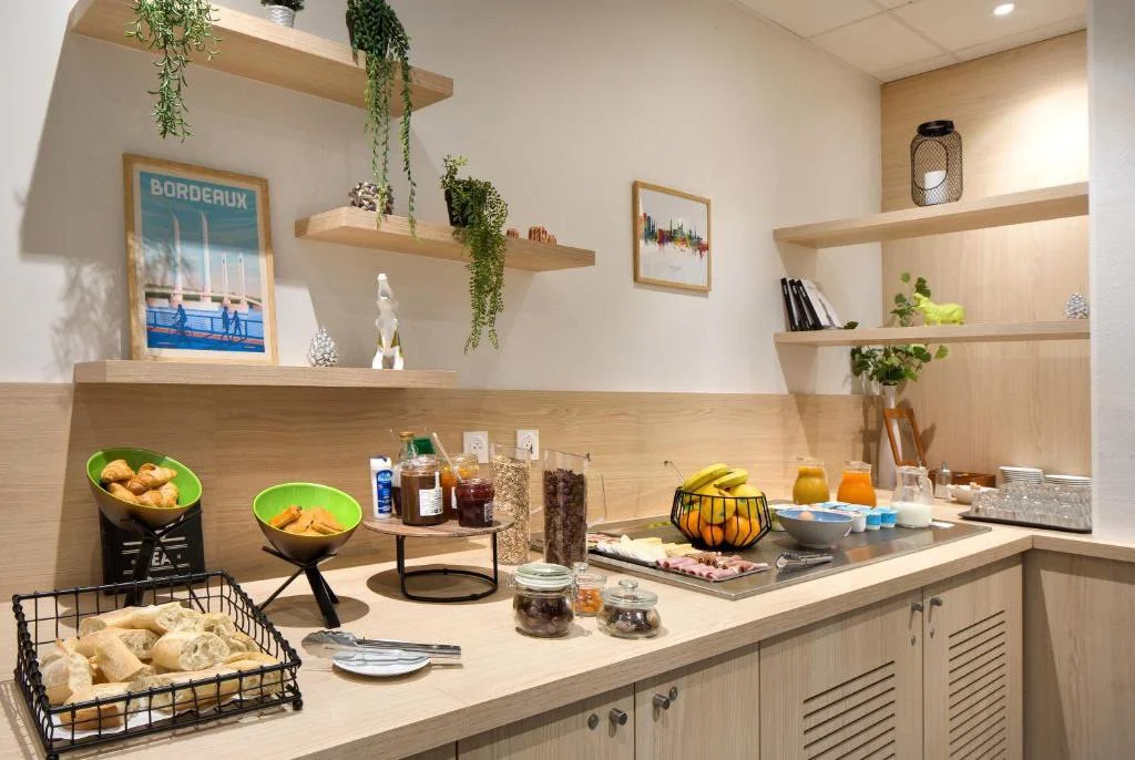 Petit-déjeuner avec fruits, confitures, viennoiseries, jus d'orange, lait, et articles de petit-déjeuner sur une comptoir de cuisine moderne en bois clair.