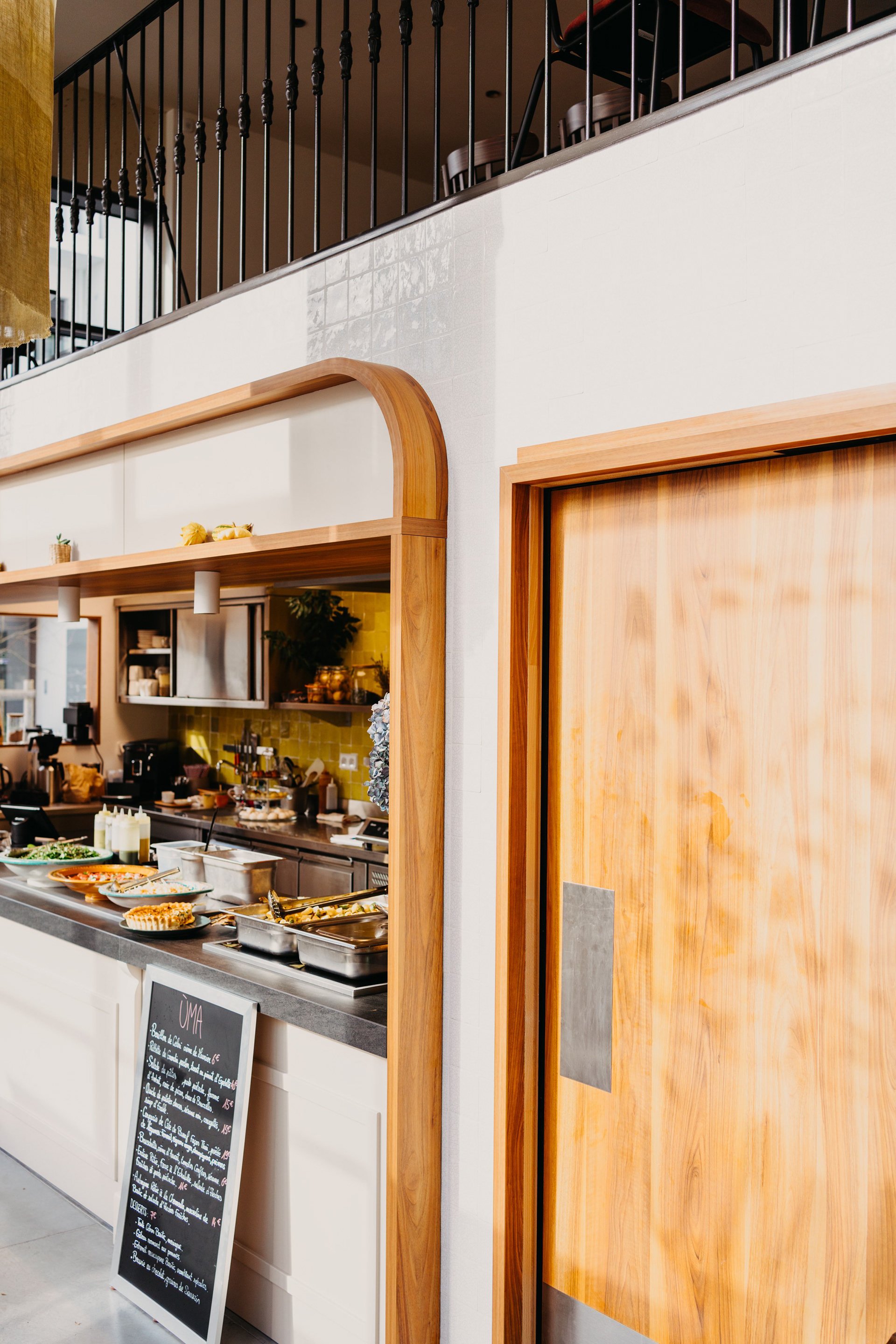 Buffet de petits-déjeuners dans une cuisine de restaurant, avec assiettes de nourriture, ardoise avec menu, et comptoir en acier inoxydable.