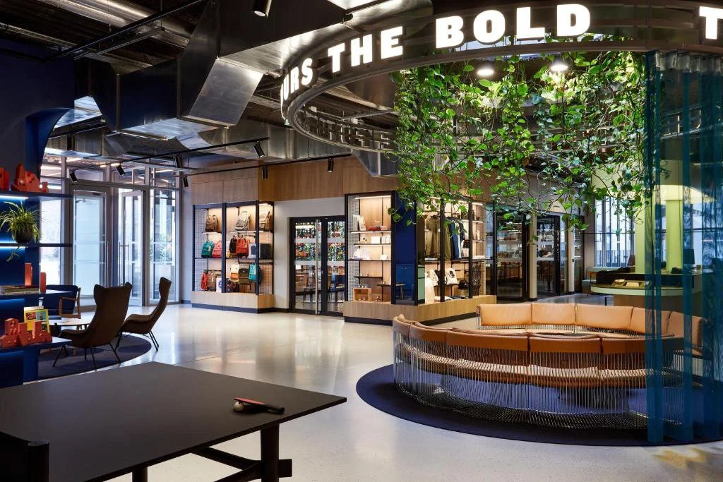 Intérieur moderne d'une boutique avec un espace de repos, étagères de produits, un arbre décoratif et une enseigne lumineuse en français.