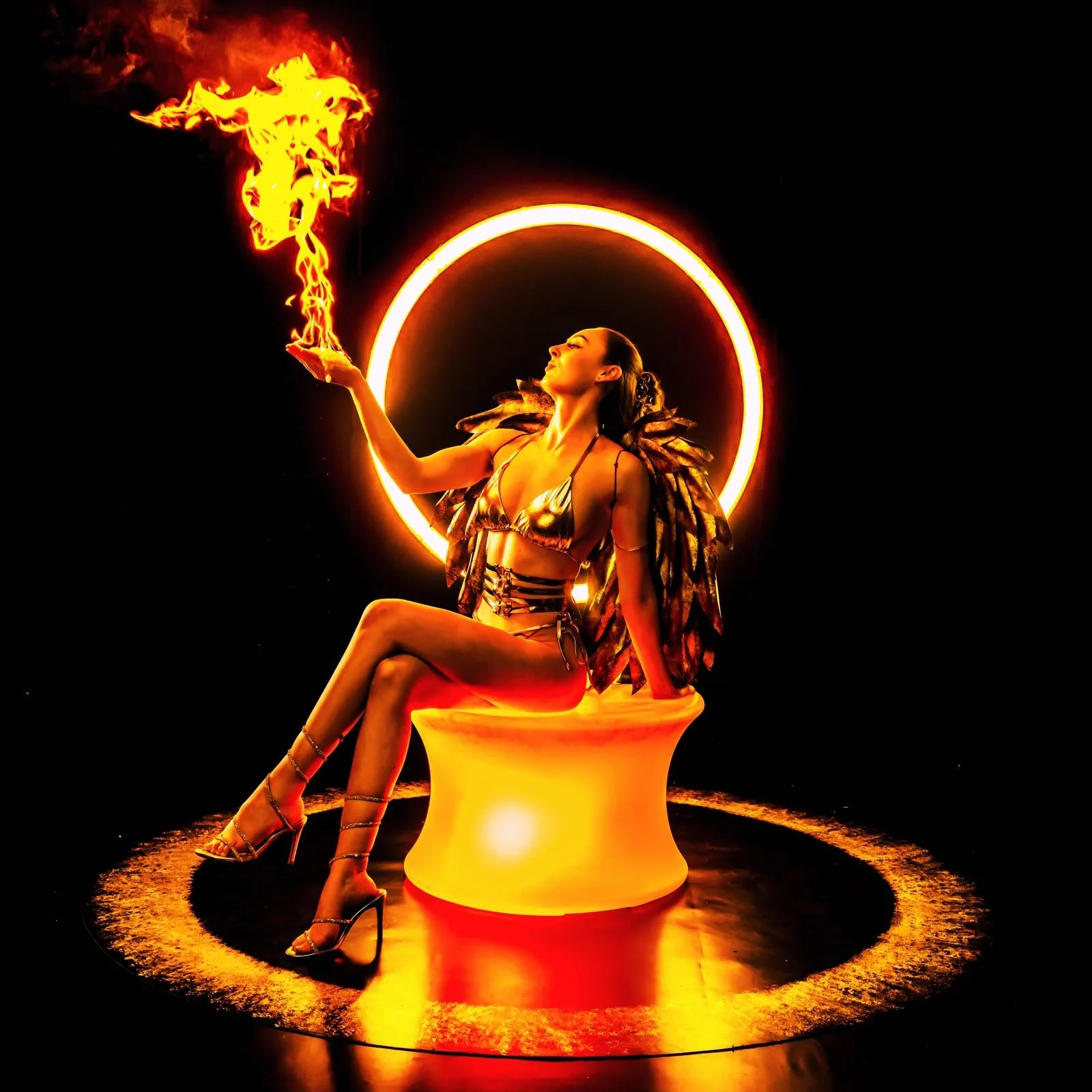 A woman sitting on a glowing orange chair, holding a torch with flames, surrounded by a circular light, with dark background.