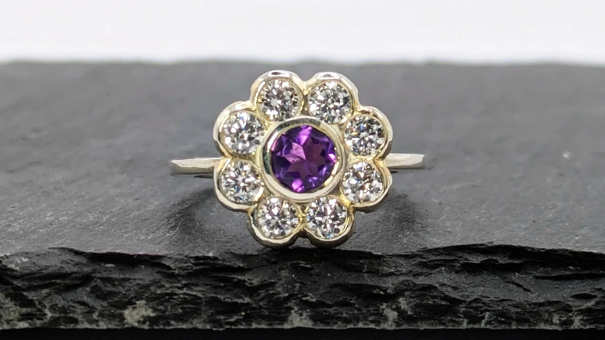 Flower. An 18ct white gold flower halo ring, featuring a central amethyst and accent moissanites. A classic design with a modern twist.