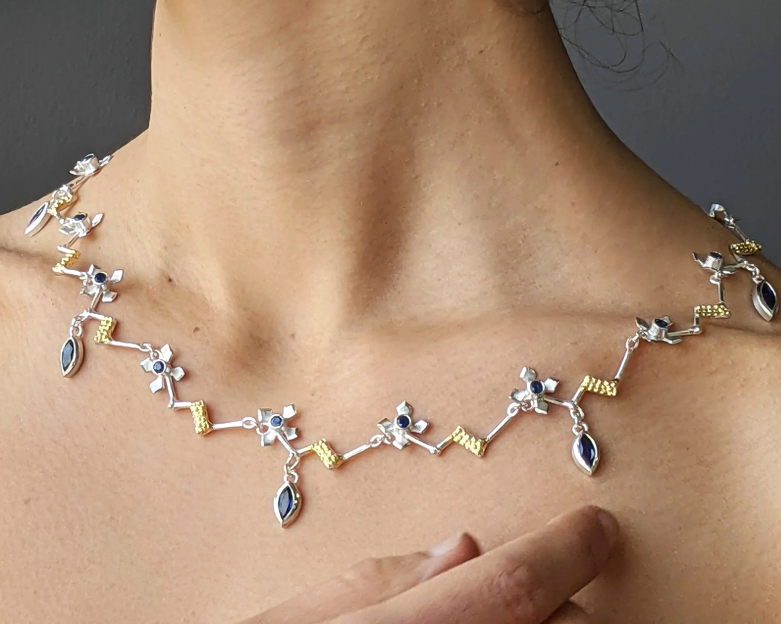 A delicate silver, gold and sapphire neck-piece that combines floral and geometric designs.