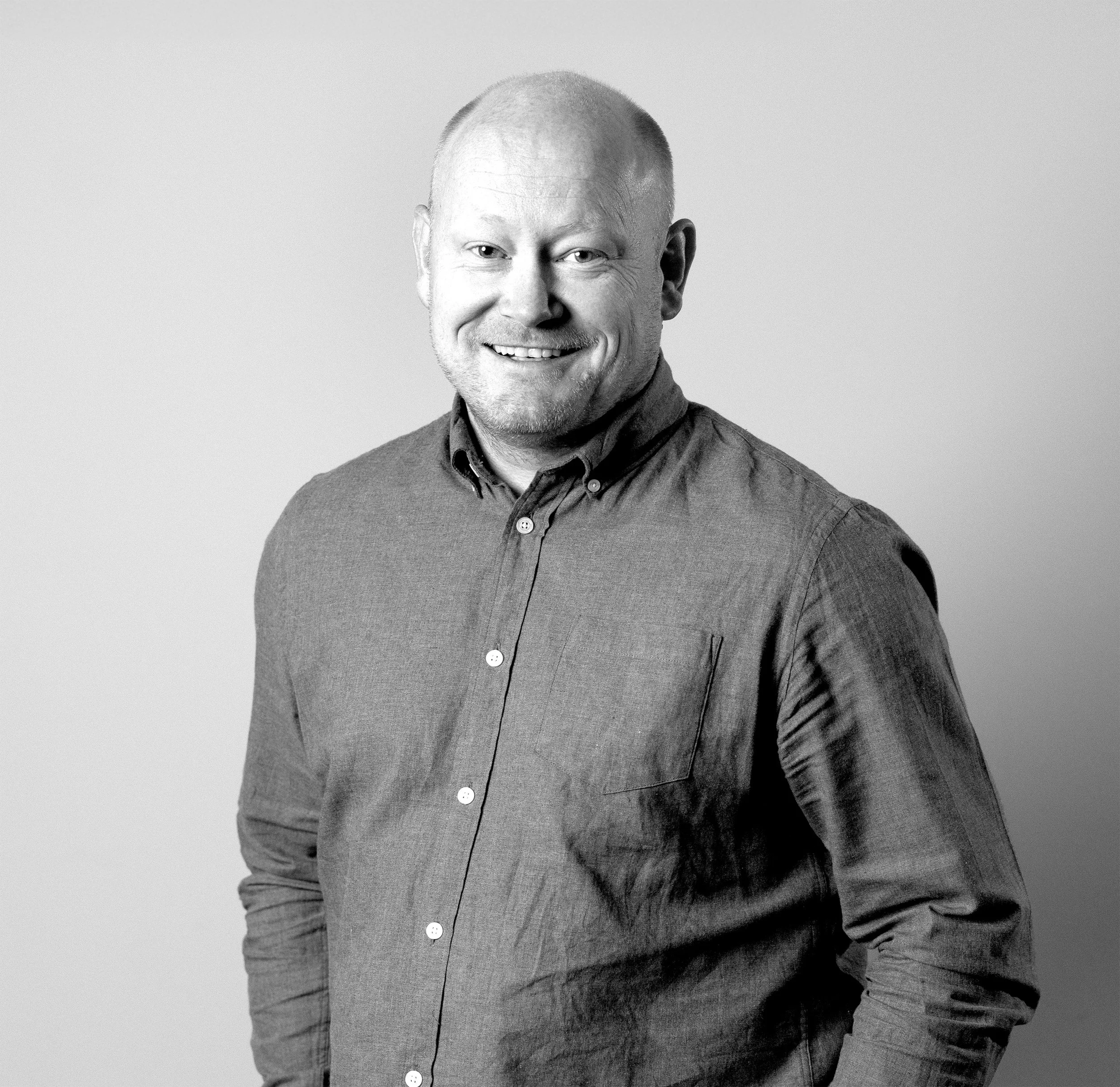 Sort/hvitt portrett av en mann med nær portrett, viser ansikt, skulder og øvre klede, smilende.