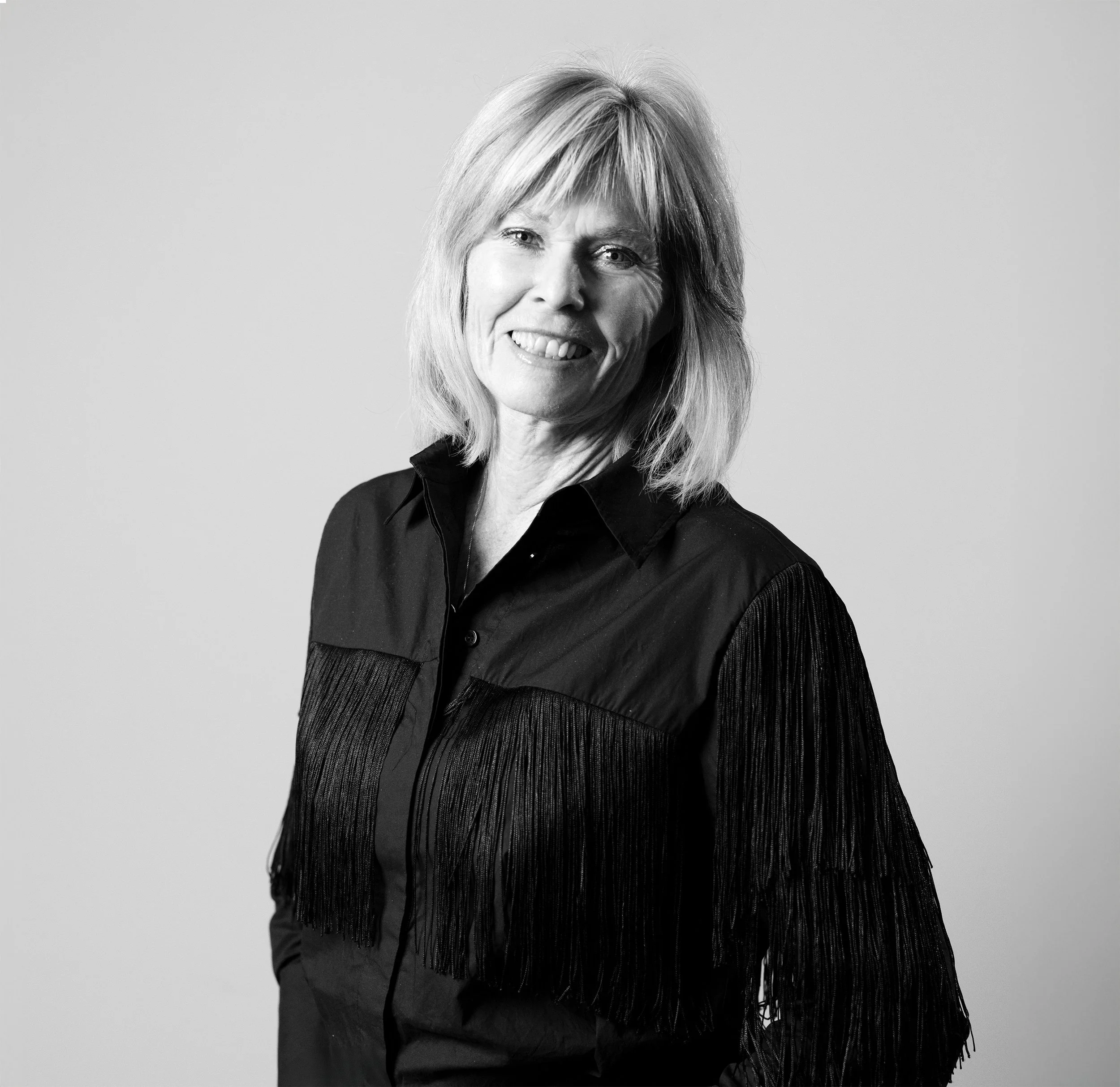 Et svart-hvitt bilde av en smilende kvinne med blondt hår, iført en svart skjorte.