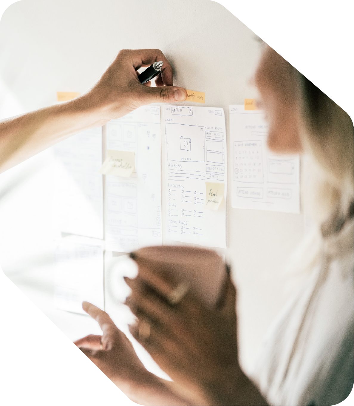 To personer som jobber med å lage en design skisse eller wireframe på en vegg, med kommentarer på post-it lapper.