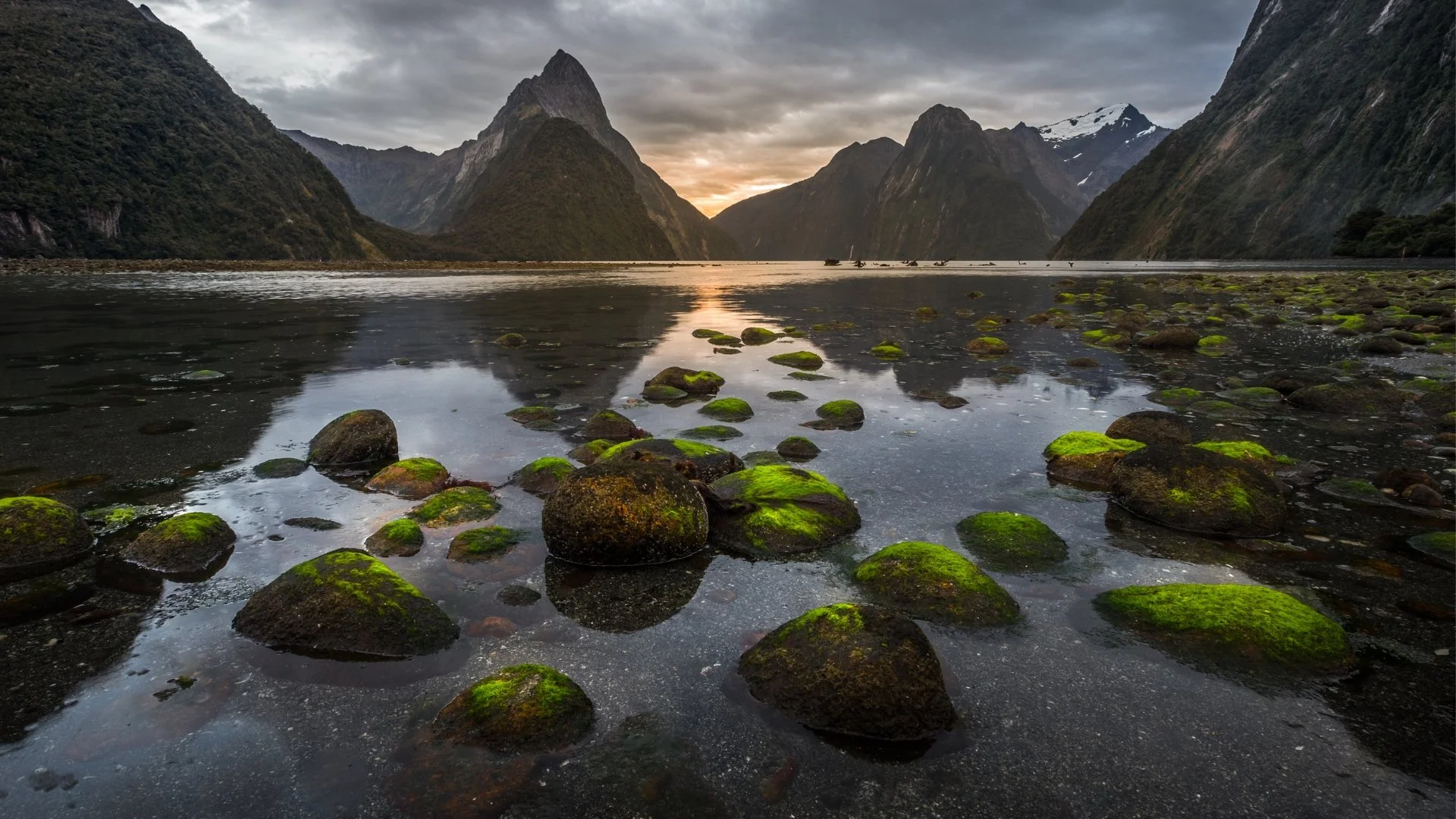 Cove with green moss-covered rocks in a river surrounded by rocky mountains under a cloudy late-afternoon sky.