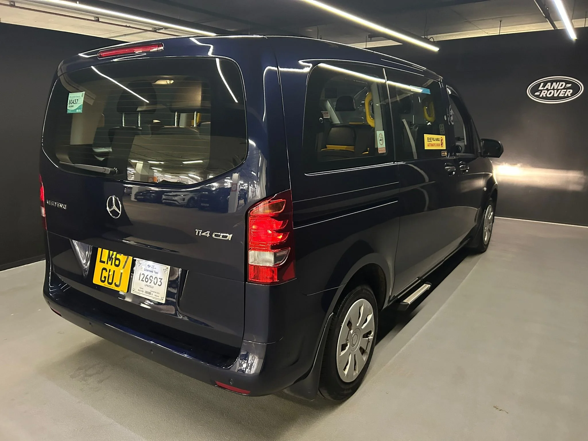 Black Mercedes-Benz Metris van in an indoor parking garage with Land Rover logo on the wall