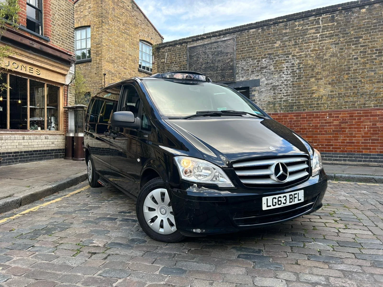 Black Mercedes-Benz van parked on a cobblestone street in front of brick and stone buildings.