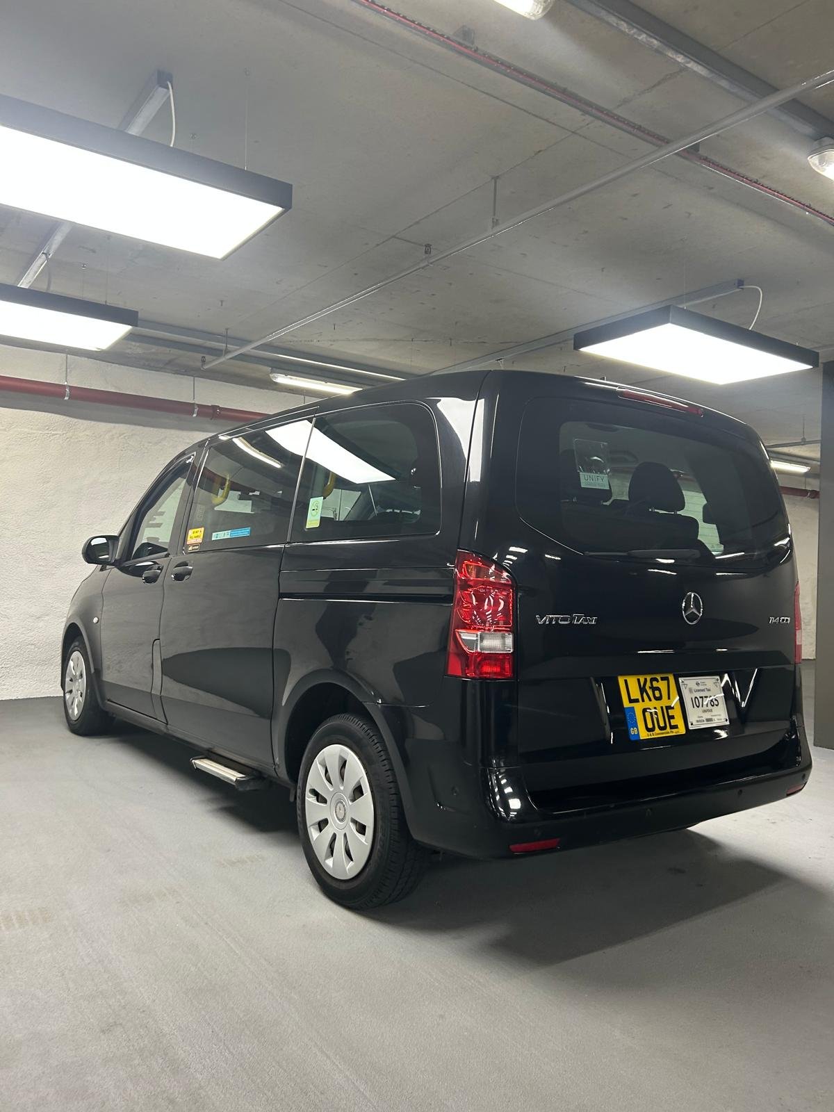 Black Mercedes-Benz Vito van parked in an indoor parking garage with fluorescent ceiling lights.