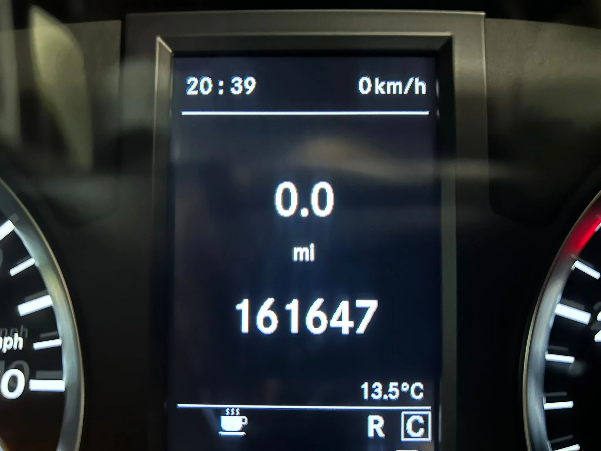 Digital car dashboard display showing time 20:39, speed 0 km/h, distance 161647 miles, temperature 13.5°C, and various icons including a coffee cup and gear shift indicator.