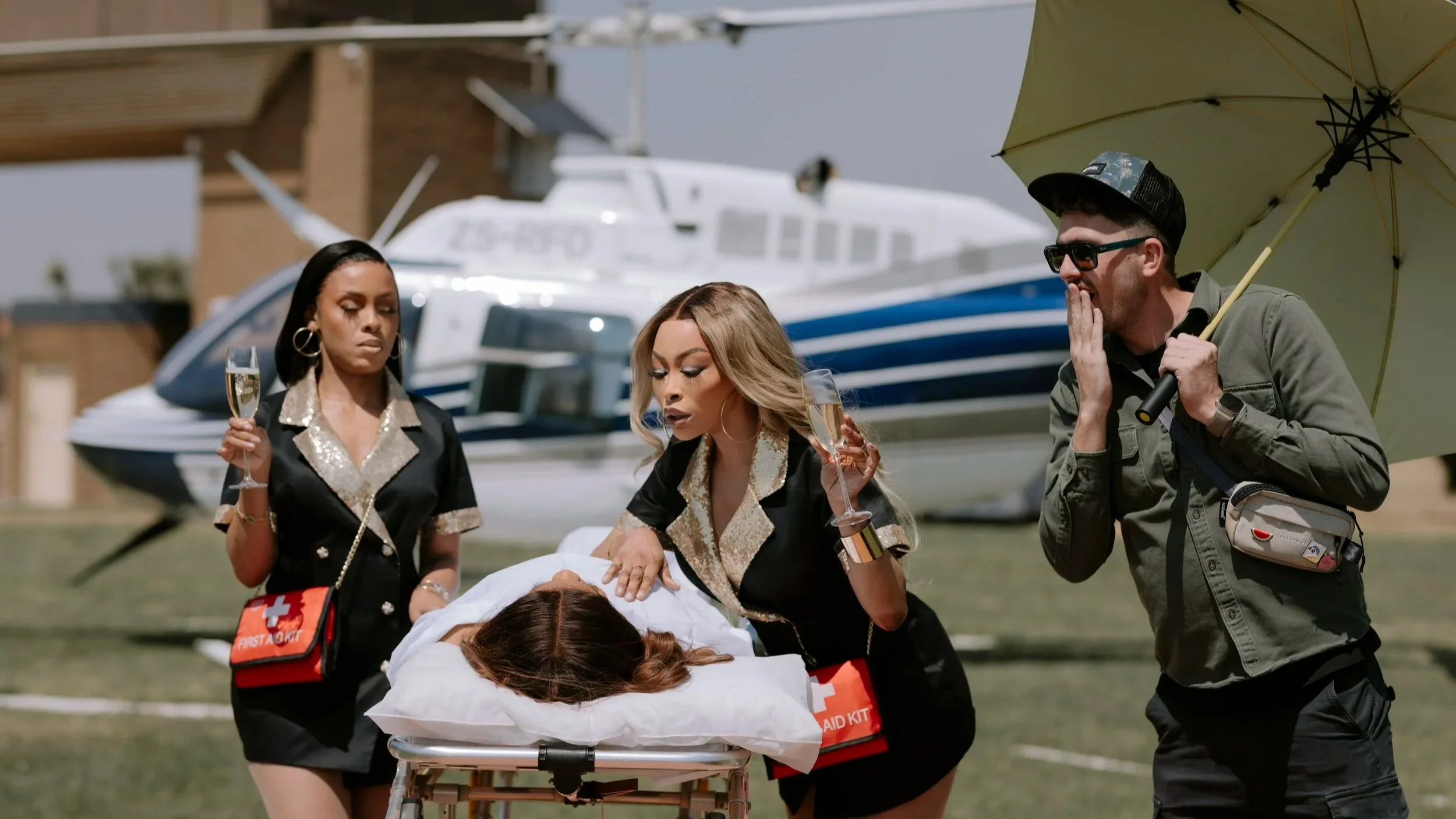 Scene of two women and a man providing emergency medical assistance to a woman lying on a stretcher with a helicopter in the background.