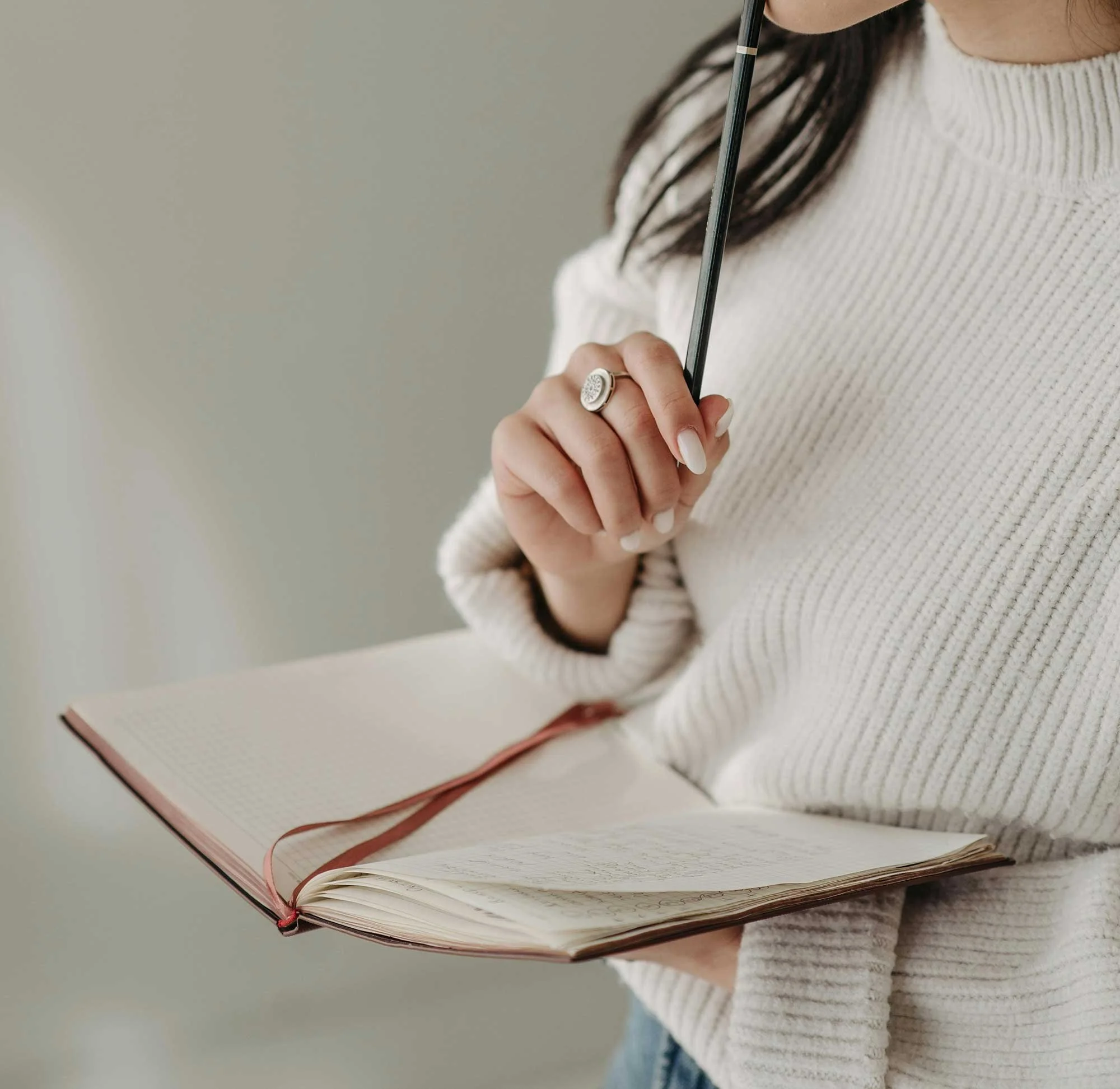 A London therapist wearing a white sweater holding an open notebook and a pen.
