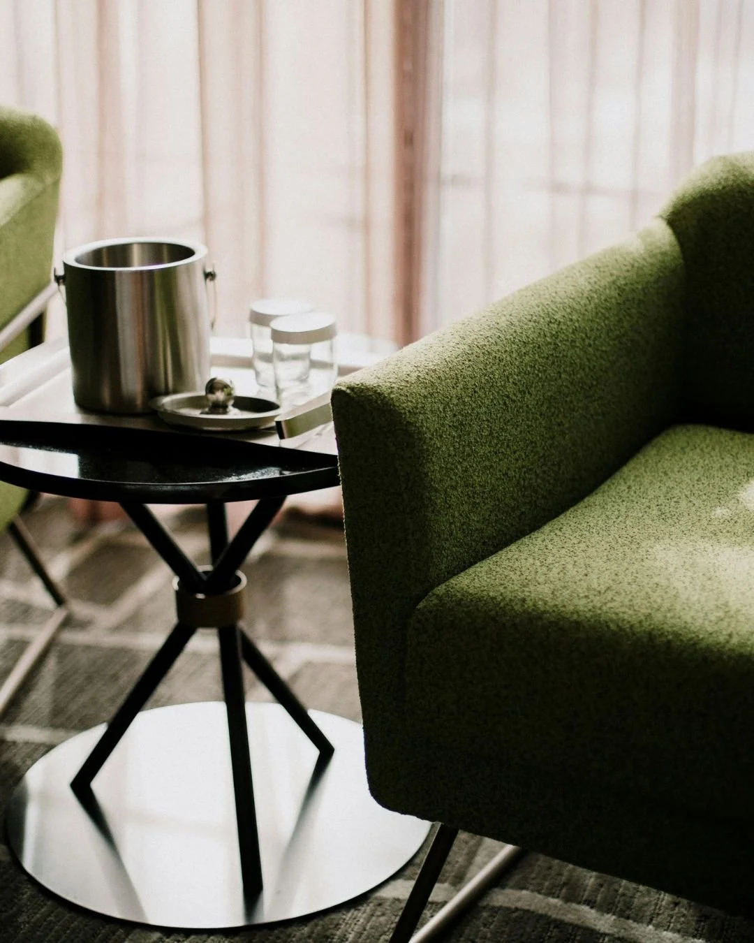 A London therapy office, with a green upholstered armchair facing the table, with a pink curtain in the background.