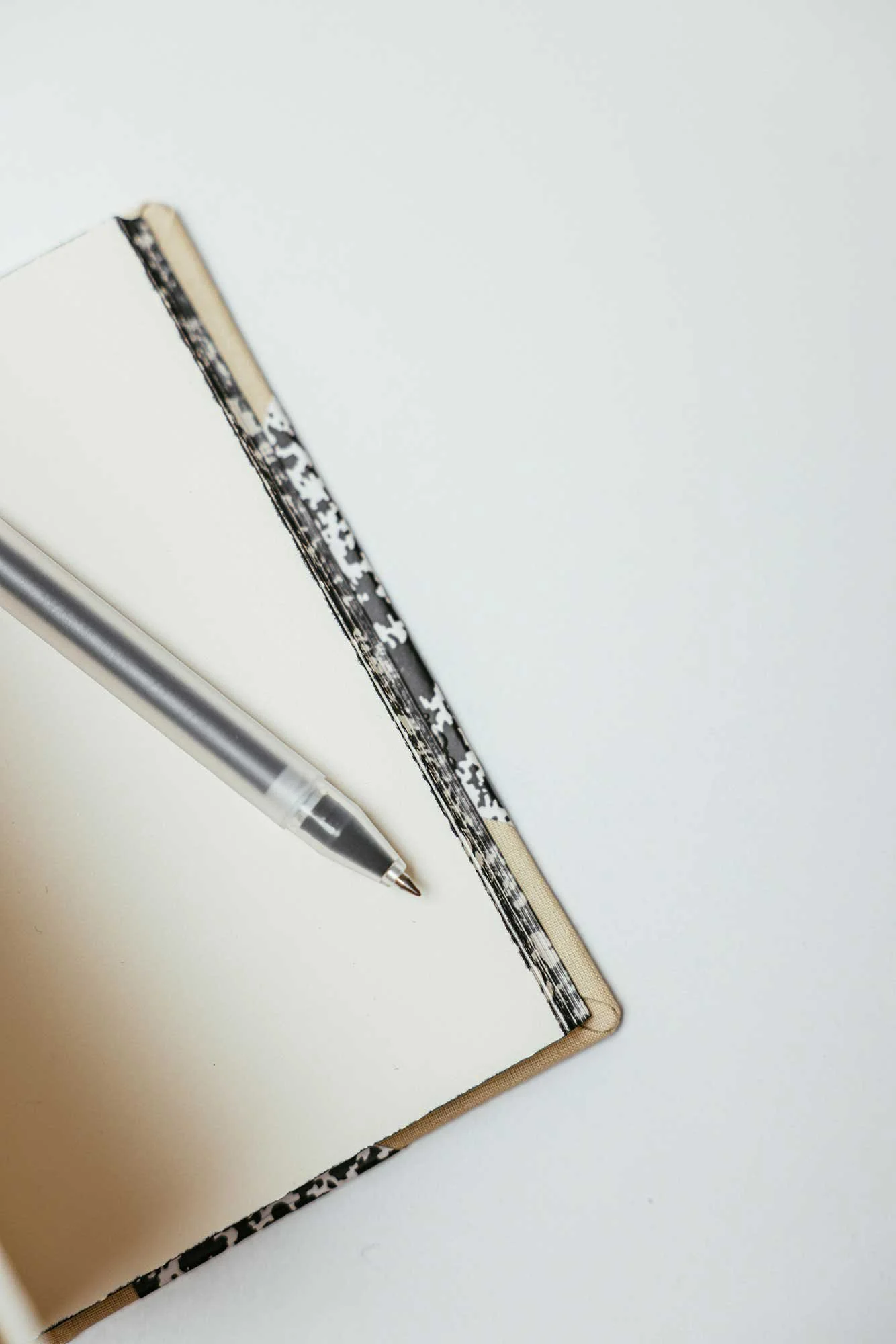 A notebook with a black and white patterned cover, a transparent ballpoint pen, and a black and white patterned pen on a white surface.
