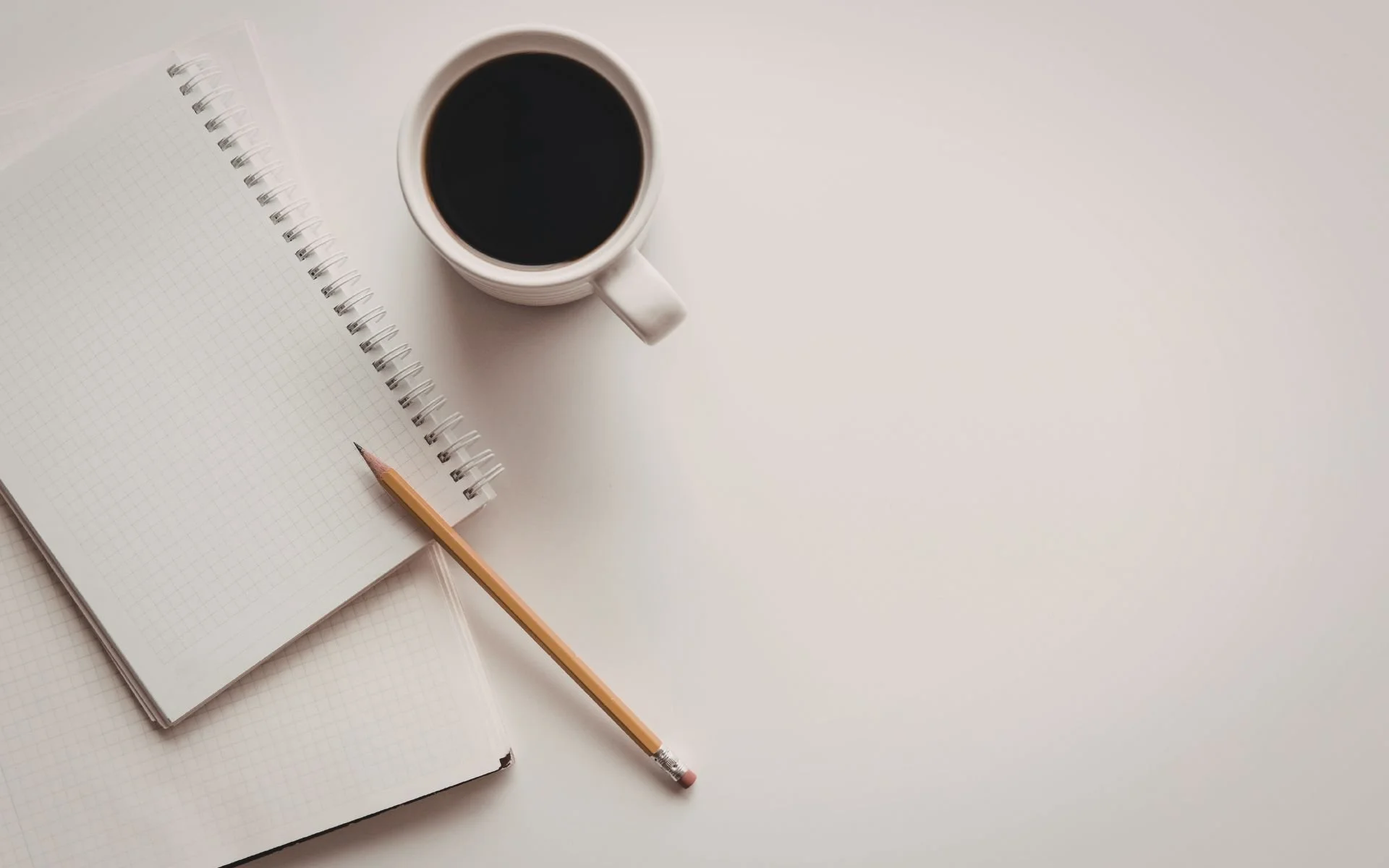 A therapist office in central London - Open notebook with graph paper pages, a pencil, a cup of black coffee, and a closed notebook on a white surface.
