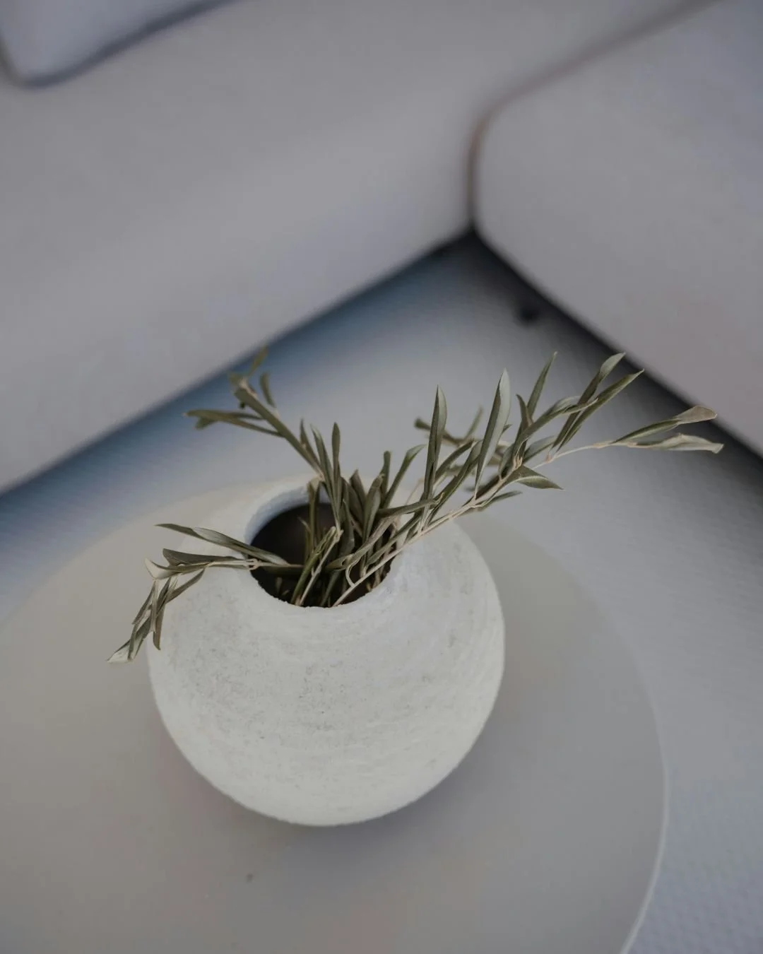 A small, round, white textured vase holding dried olive branches, in a discreet, central London therapy office