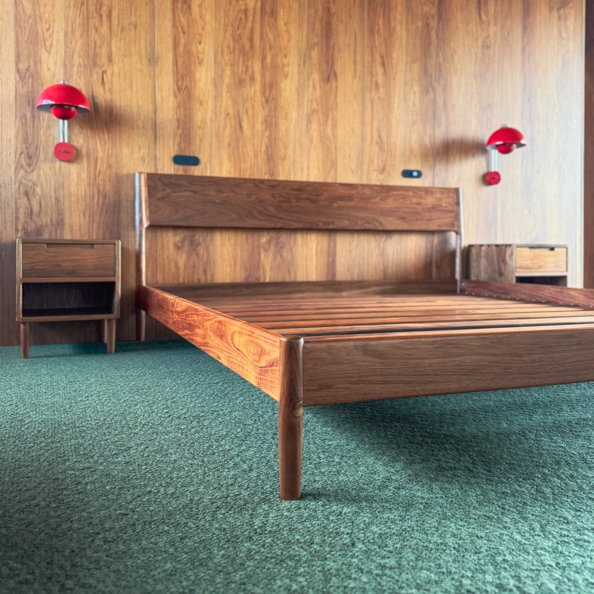 Wooden church pew with red wall-mounted lamps on a green carpeted floor.