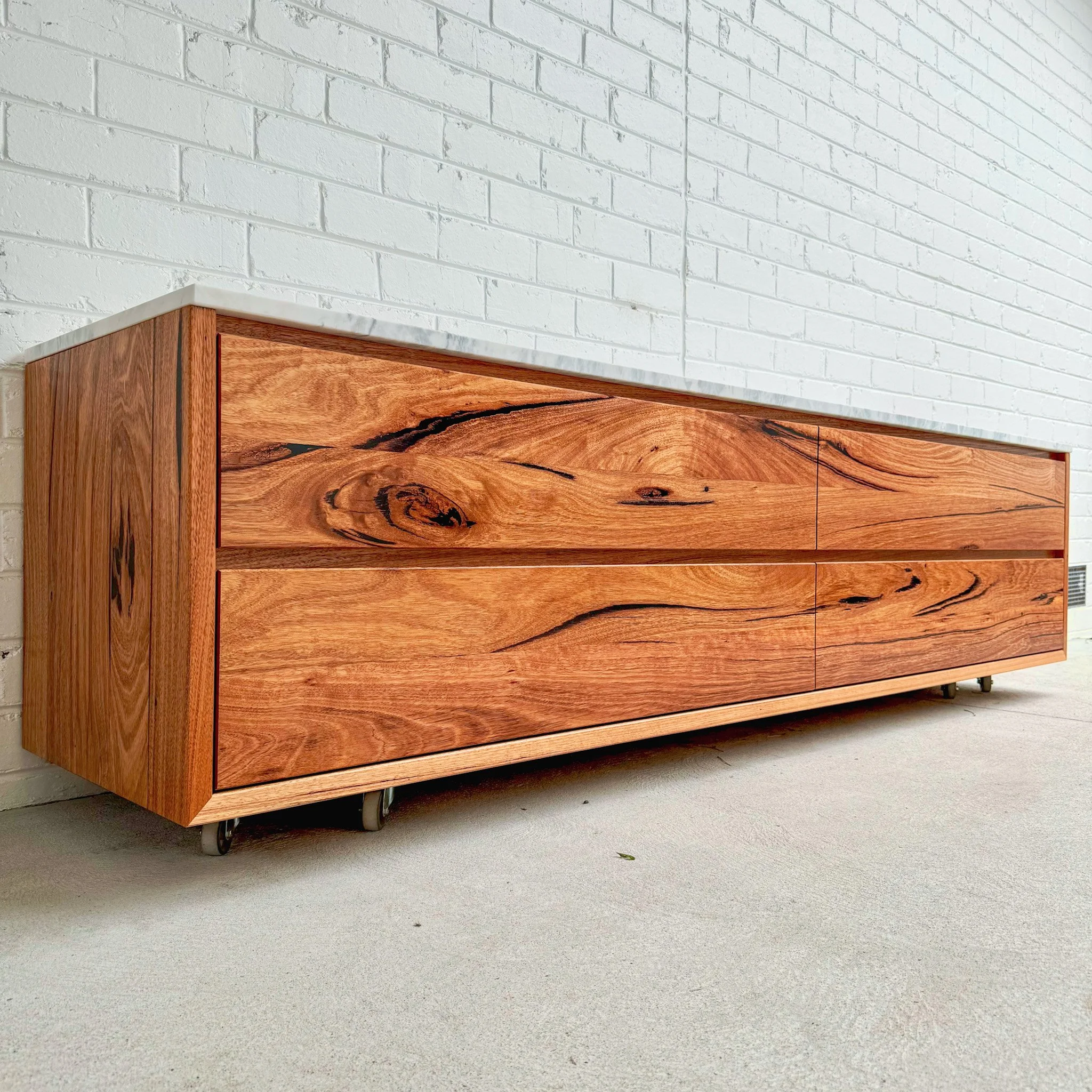 Wooden cabinet on wheels against a white brick wall and gray concrete floor.
