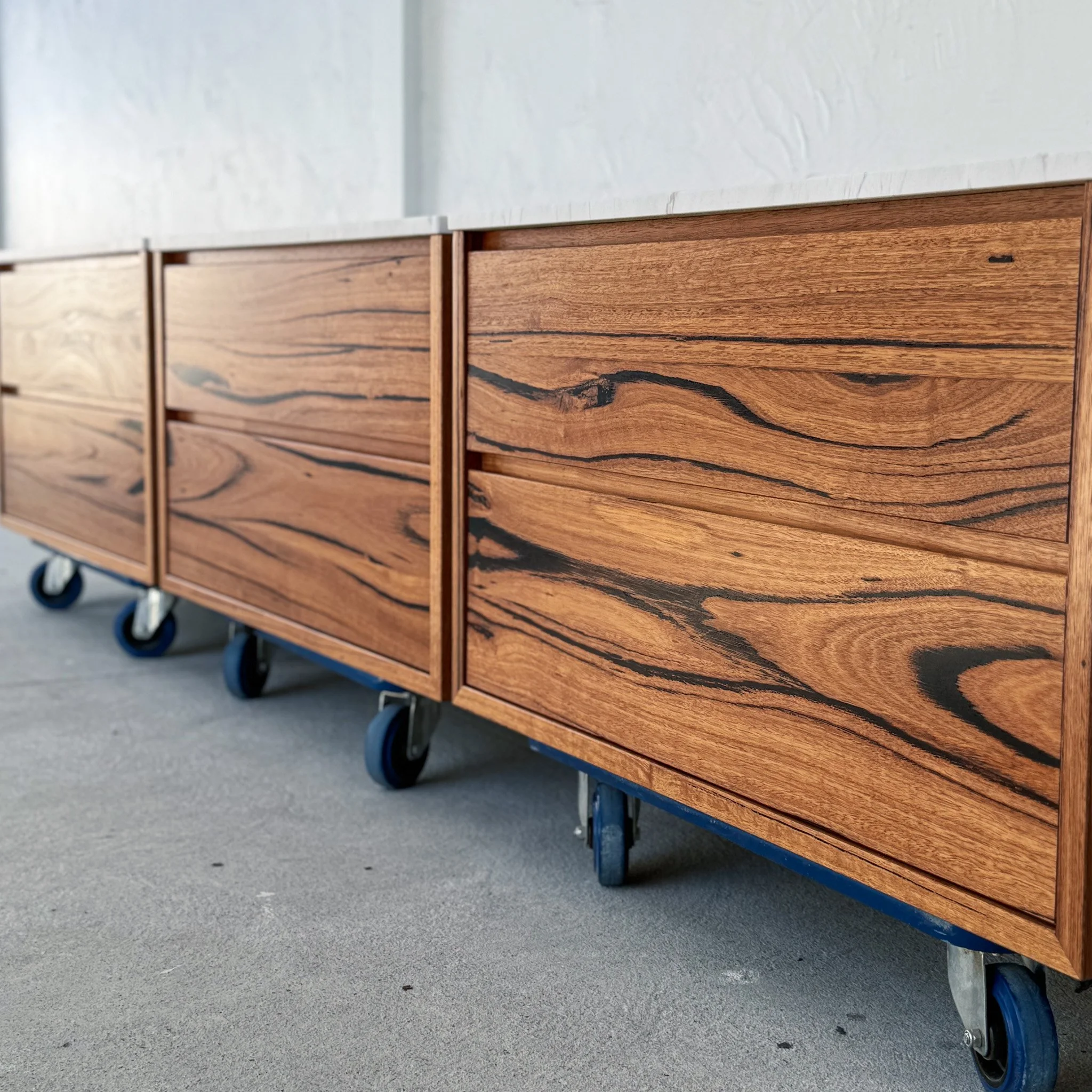 Close-up of a wooden dresser with multiple drawers on a gray concrete floor, with visible caster wheels at the bottom.
