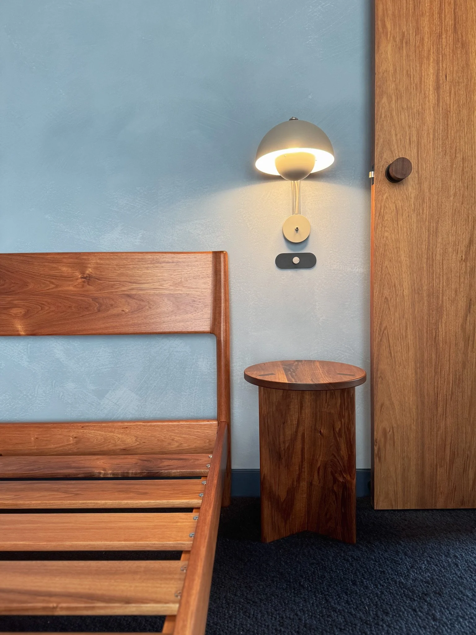Interior room corner with wooden paneling, a small wooden side table, an abstract wall lamp, and a blue wall background.