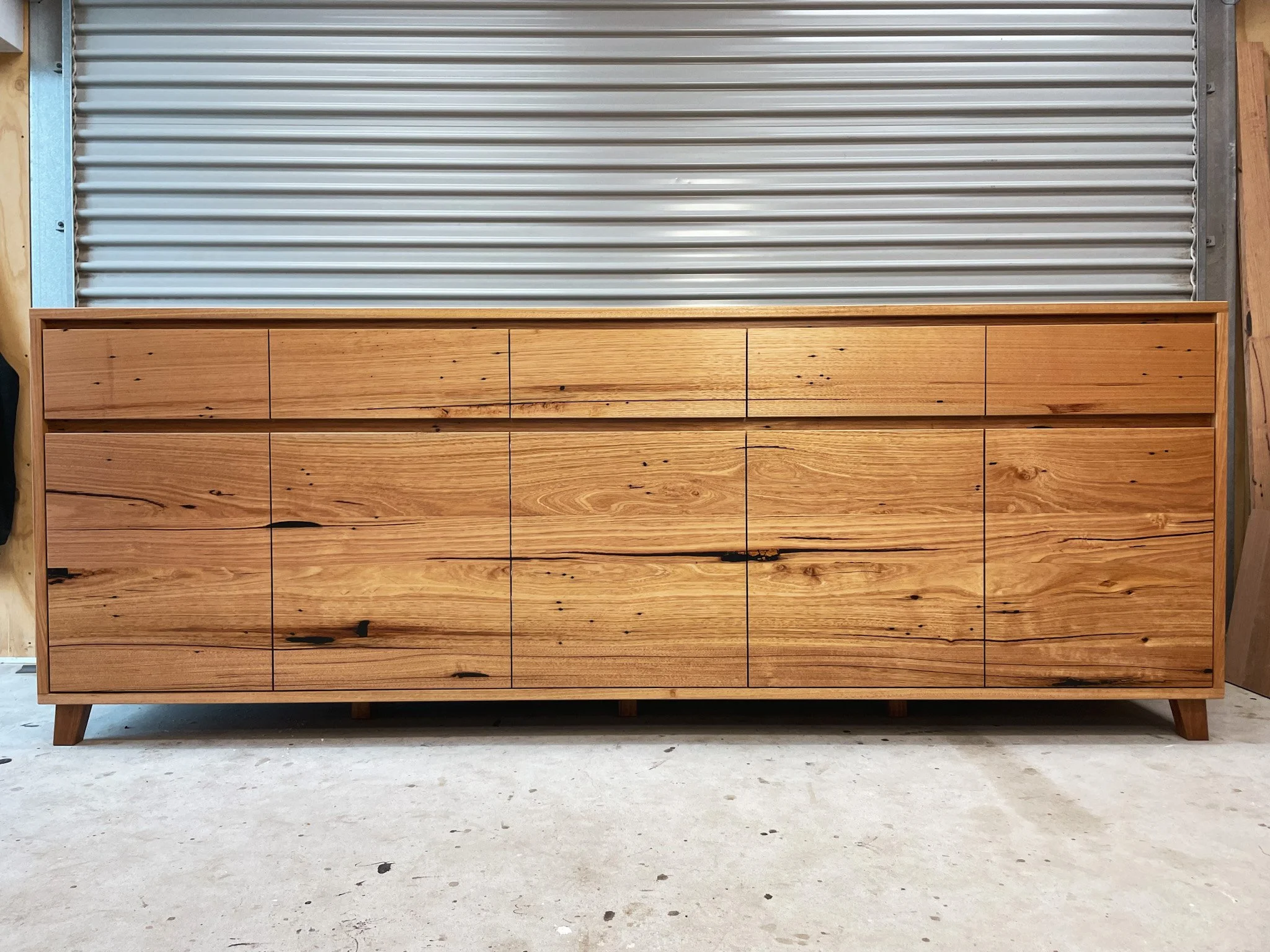 A large wooden dresser with multiple drawers and a mid-century modern design stored in an unfinished room.