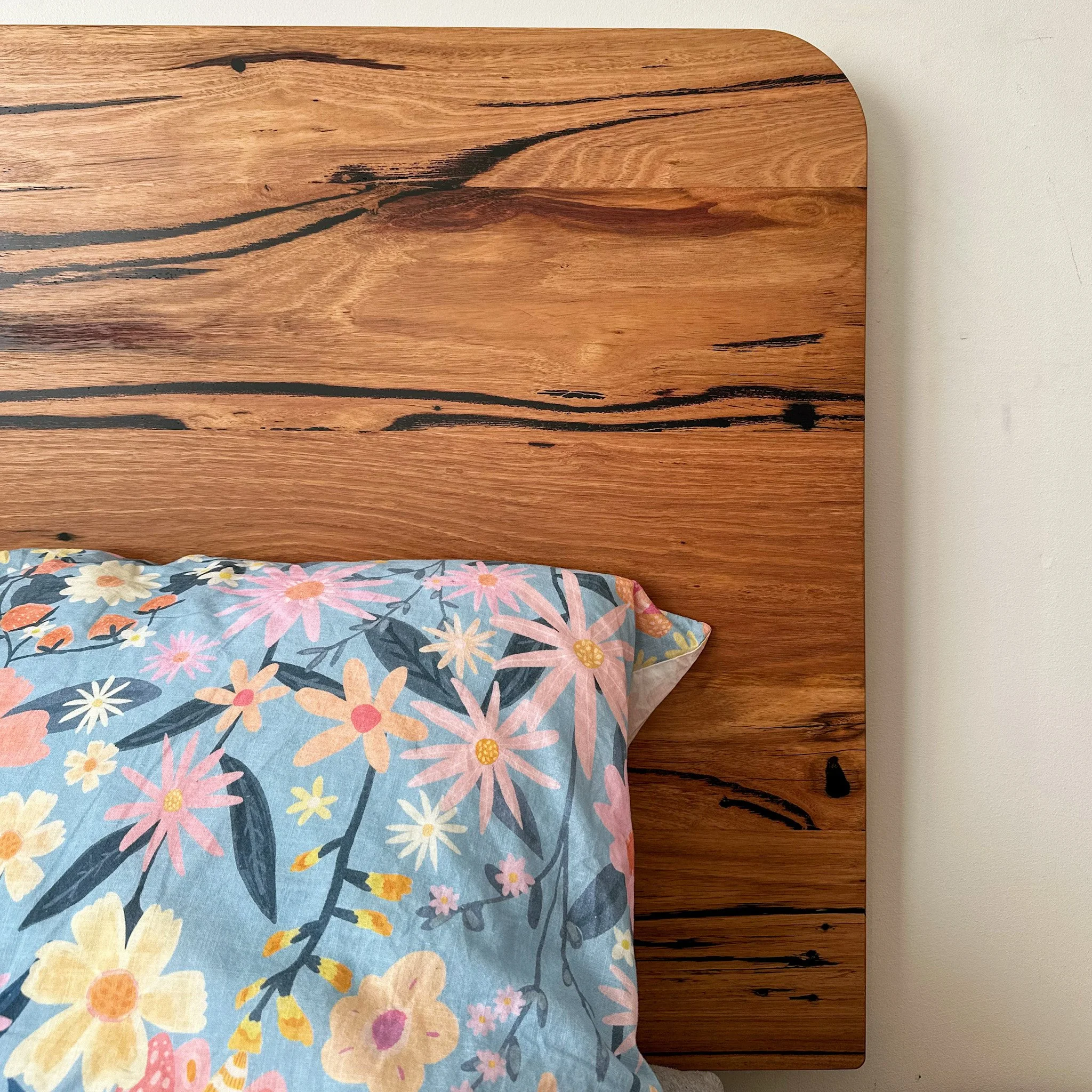 Close-up of a wooden headboard with black streaks and grain patterns, shown above a bed with a floral bedspread.
