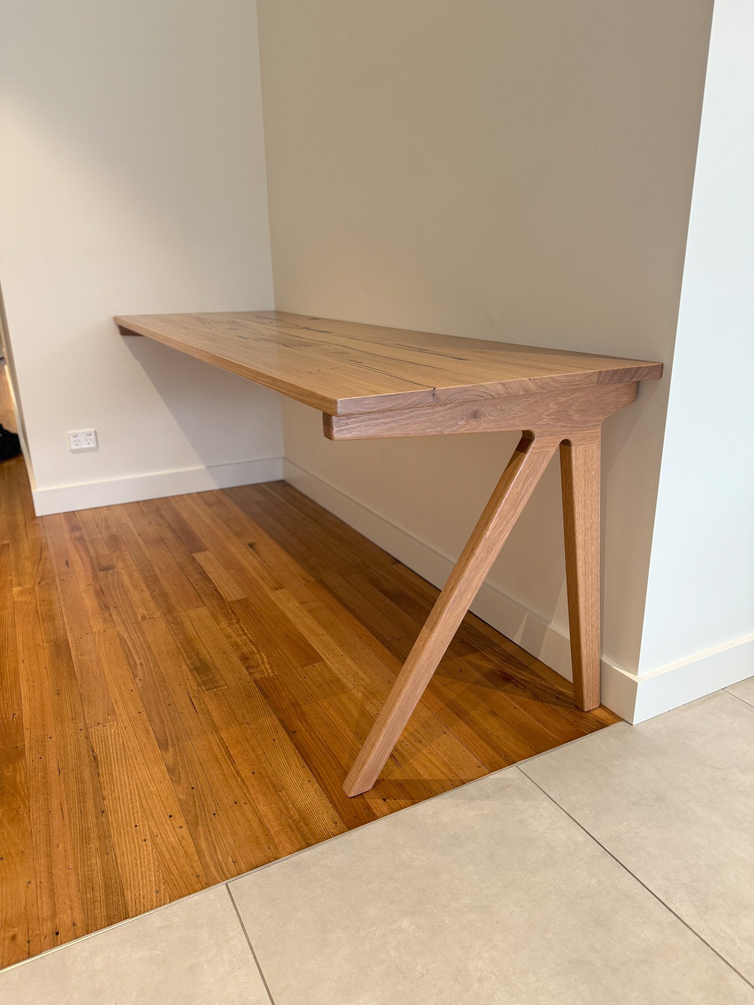 A timber desk attached to the wall in a corner, with a single leg supporting it.