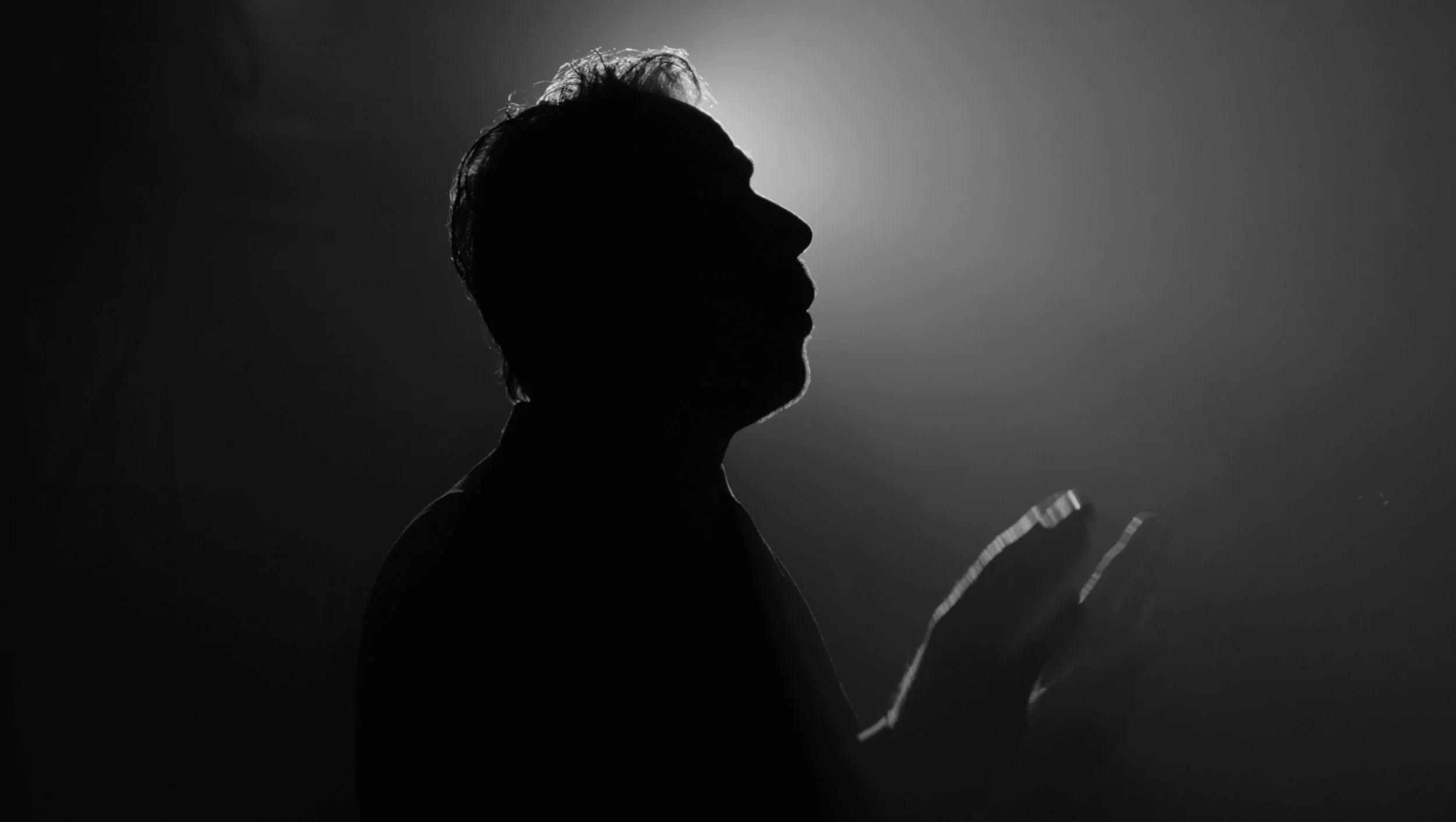 Silhouette of a man presenting on stage, backlit creating a shadowed profile against a light background.