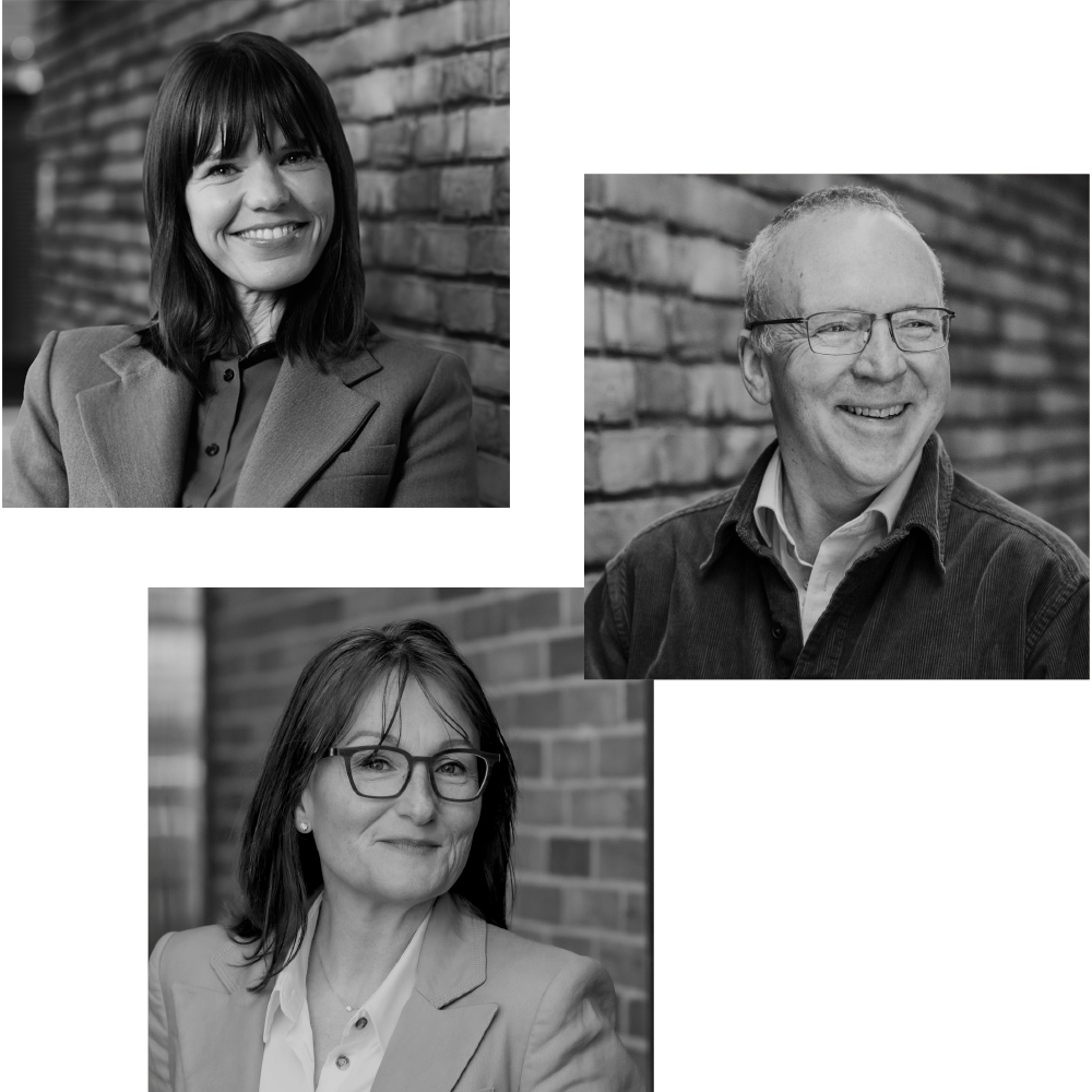 Group portrait of three professionals, two women and one man, outdoors against a brick wall, smiling.