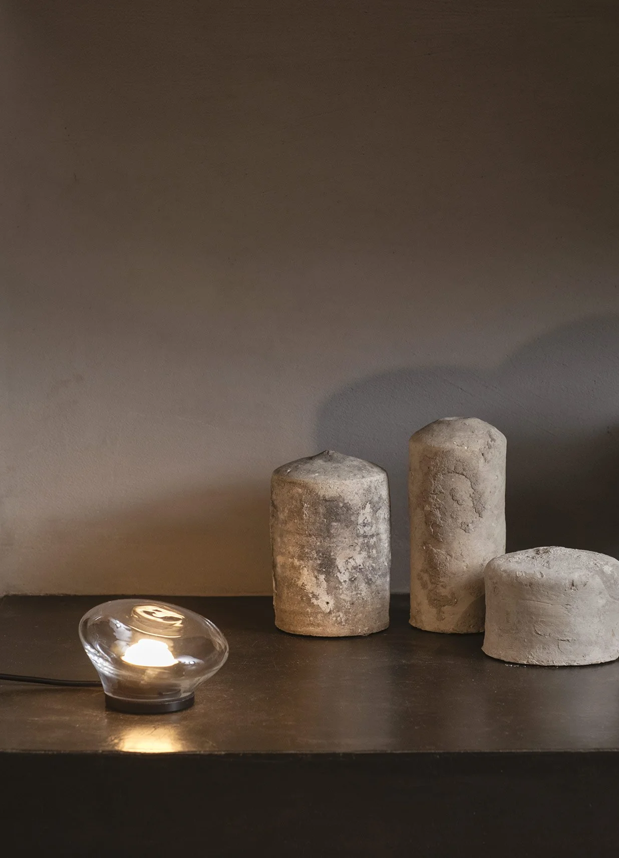 Tre candelabri di legno con candele nella parte superiore e una piastrella di vetro con candela accesa davanti a loro, su un tavolo in un ambiente domestico.