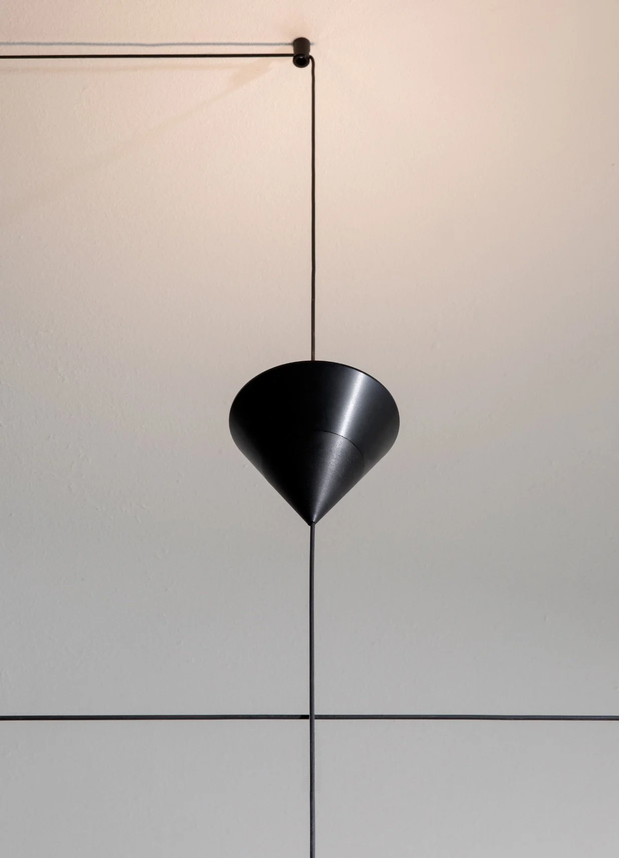 Razzo a forma di cono nero sospeso dal soffitto con fili sottili, sfondo bianco con linee nere