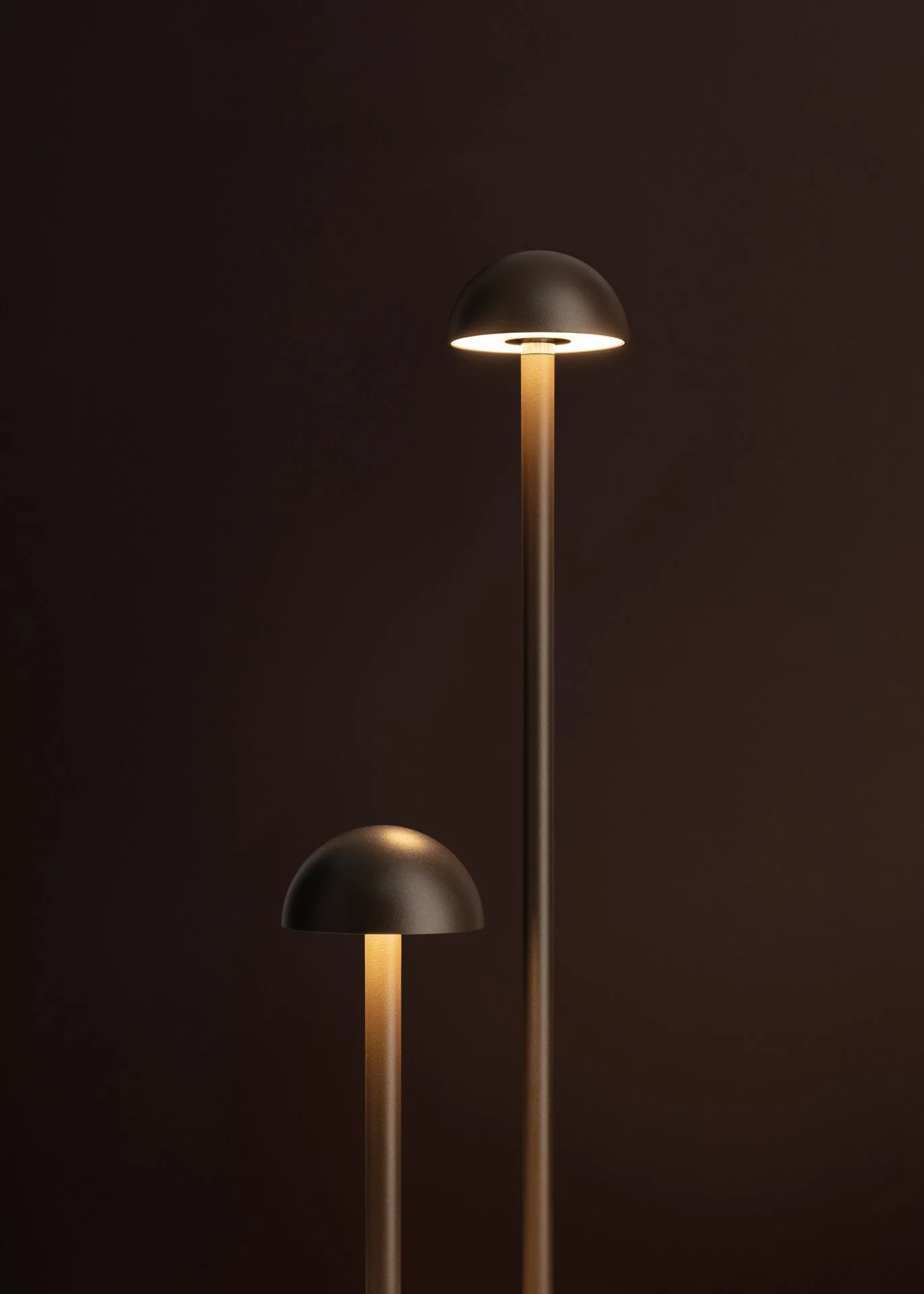 Luce da terra di design moderno con forma di cappello in nero e base in rosa dorato, ambientata su sfondo scuro.