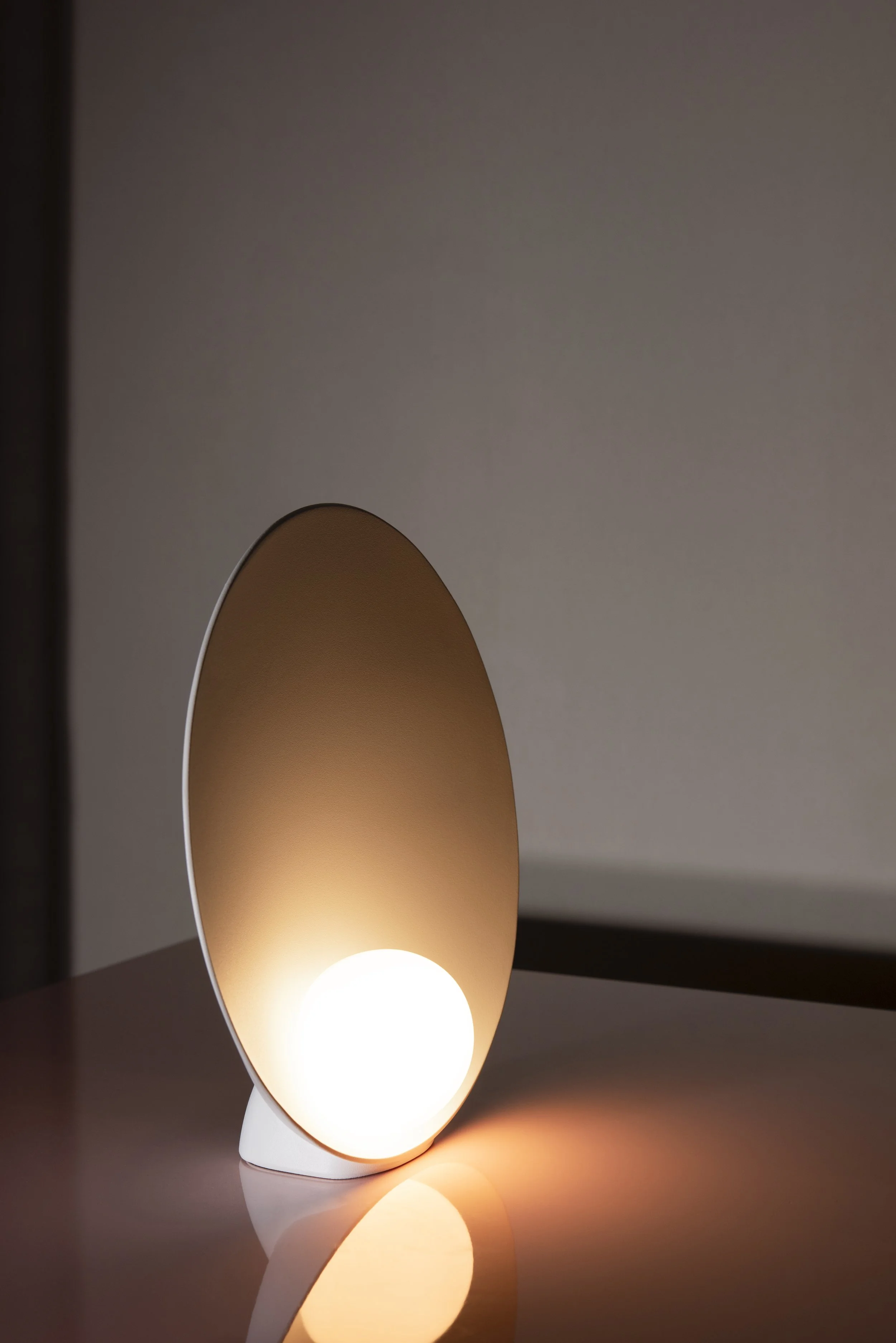 Una lampada moderna con una forma idromassaggio, emette una luce calda e morbida, posizionata su una superficie di colore chiaro in un ambiente interno.