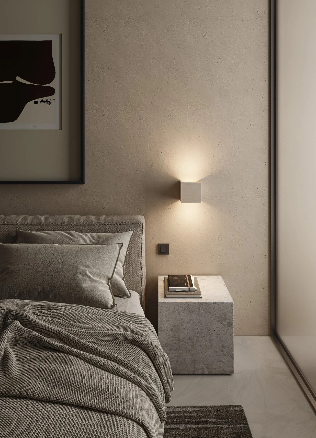 Una camera da letto moderna con pareti beige, una testiera di letto in tessuto grigio, cuscini coordinati, un tavolino in pietra con libri sopra, un'illuminazione a parete con luce calda e una porta a specchio.
