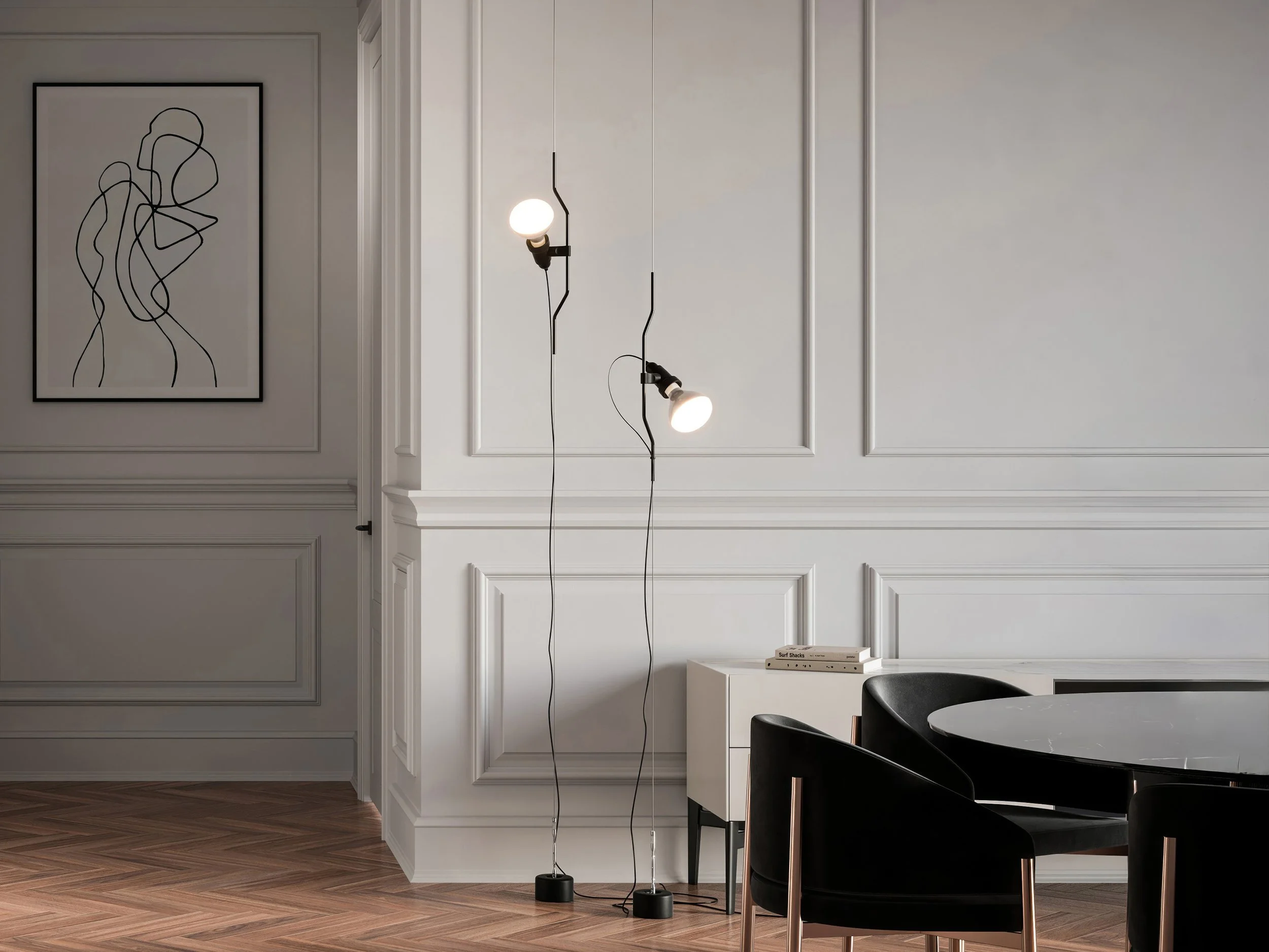 Interno di una stanza moderna con pareti bianche decorate con pannelli, un lampadario a braccio con due luci accese, un tavolo nero con sedie nere, e sopra una mensola di colore chiaro con alcuni libri.