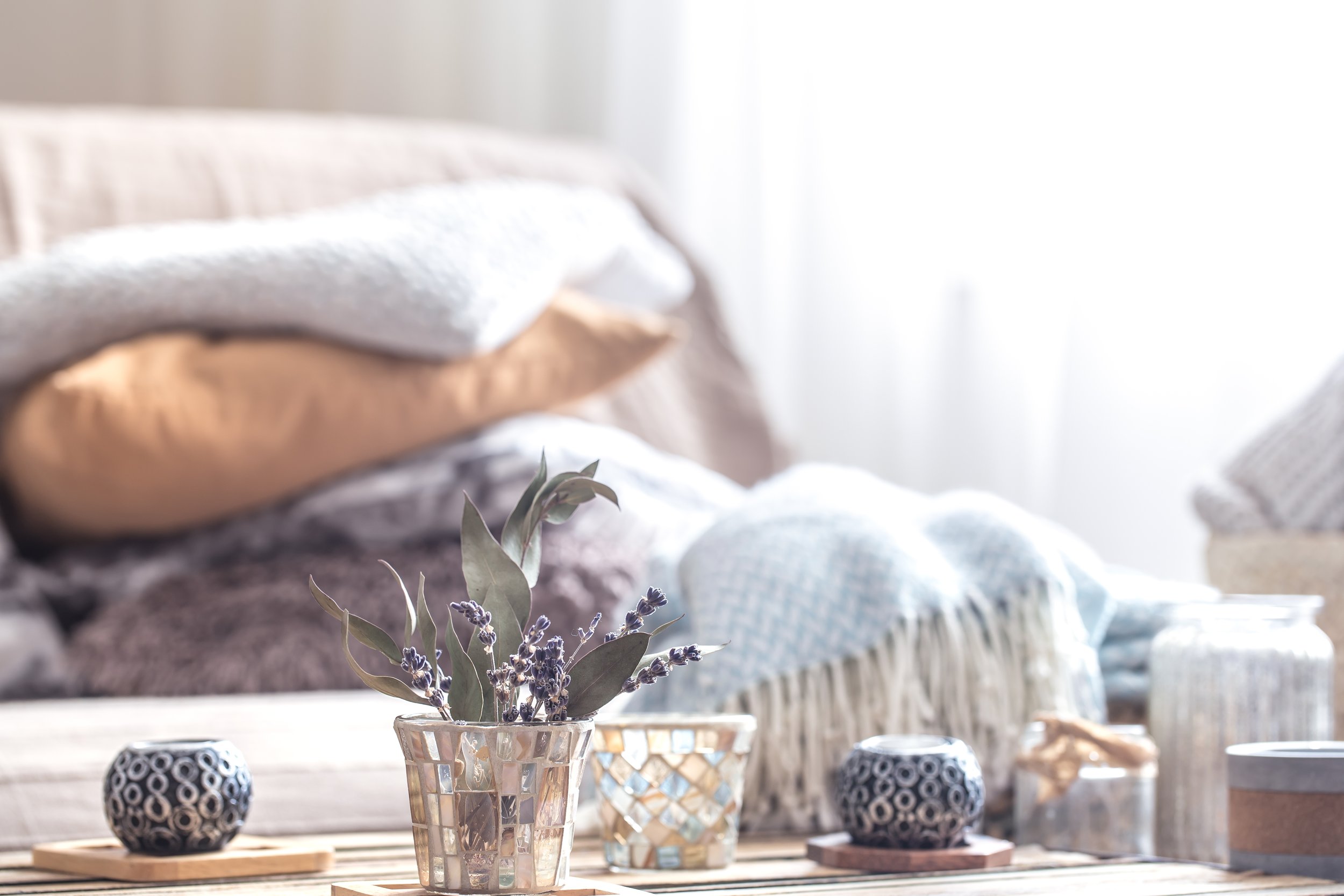 Decorative glass vases with lavender and plant arrangements on a wooden table, with a cozy, light-filled room in the background.