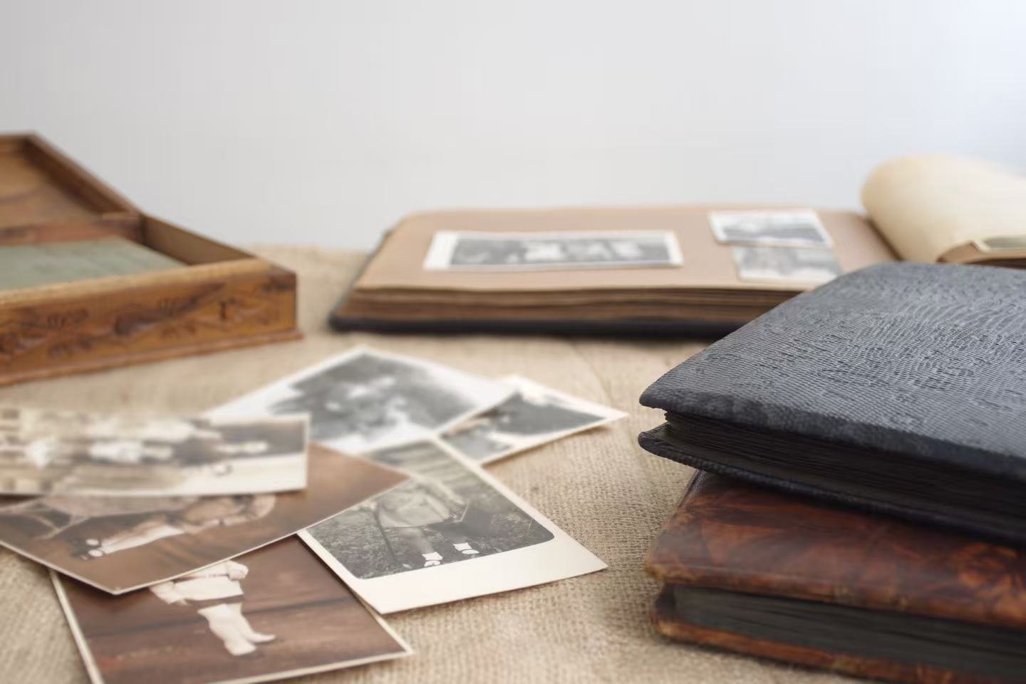 A desk with black-and-white photographs spread out, a stack of photo albums or scrapbooks, and a wooden box. The photos include family pictures and outdoor scenes.
